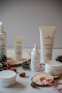 A collection of skincare products from the brand Plandae displayed on wooden rounds, accompanied by festive elements like pinecones, acorns, and candy canes. The arrangement creates a natural and holiday-themed aesthetic.