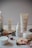 A collection of skincare products from the brand Plandae displayed on wooden rounds, accompanied by festive elements like pinecones, acorns, and candy canes. The arrangement creates a natural and holiday-themed aesthetic.