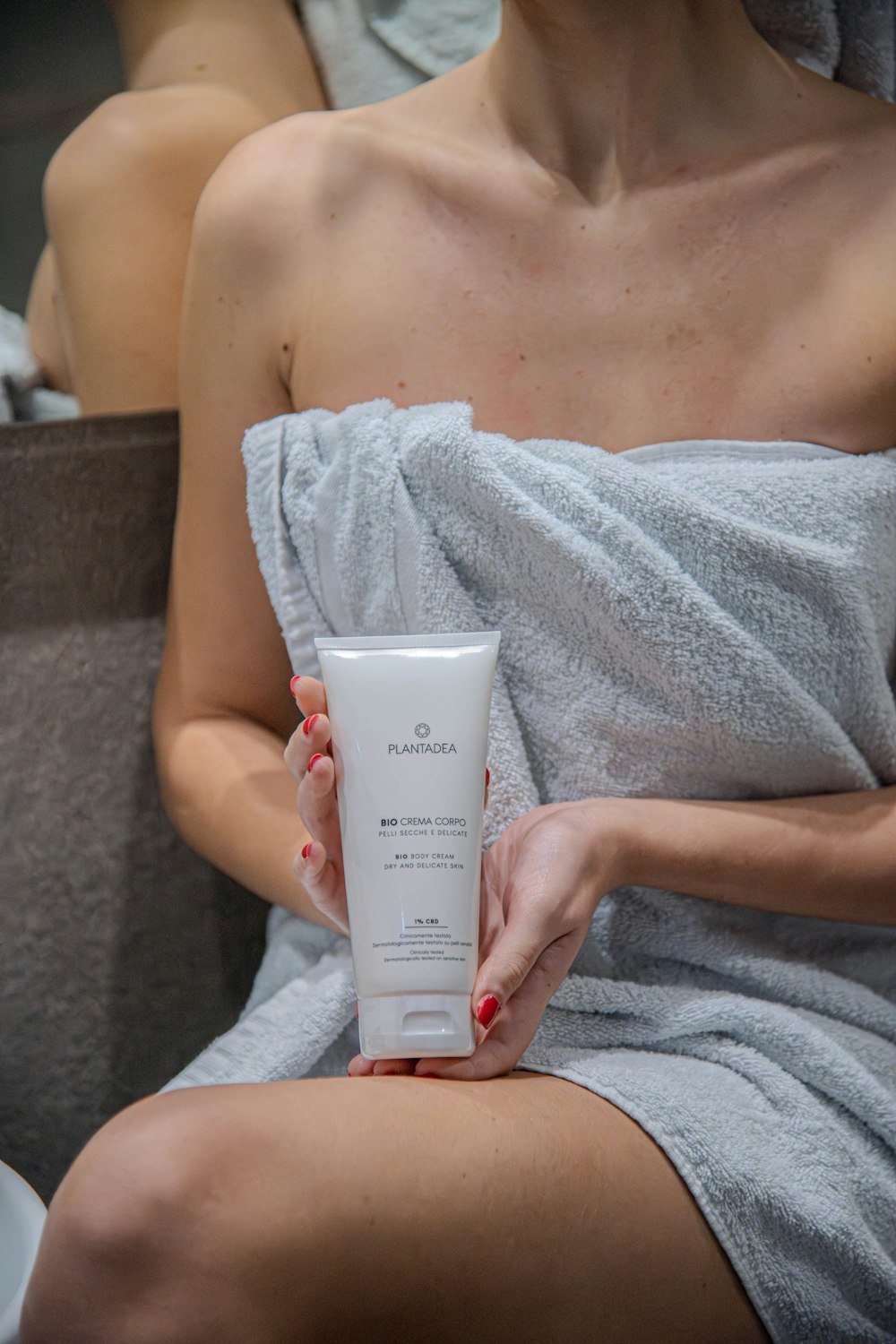 a woman in a towel holding a tube of cream