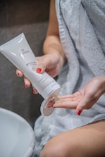A person applying cream on their nails with a calm green background.