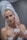 A person with a towel wrapped around their head applies a cream to their face. The individual has red nail polish and holds a jar of cream, focusing on their skincare routine in a bathroom setting.