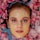 A woman's face emerges from a surface surrounded by vibrant pink rose petals, with a creamy facial mask applied to her skin.