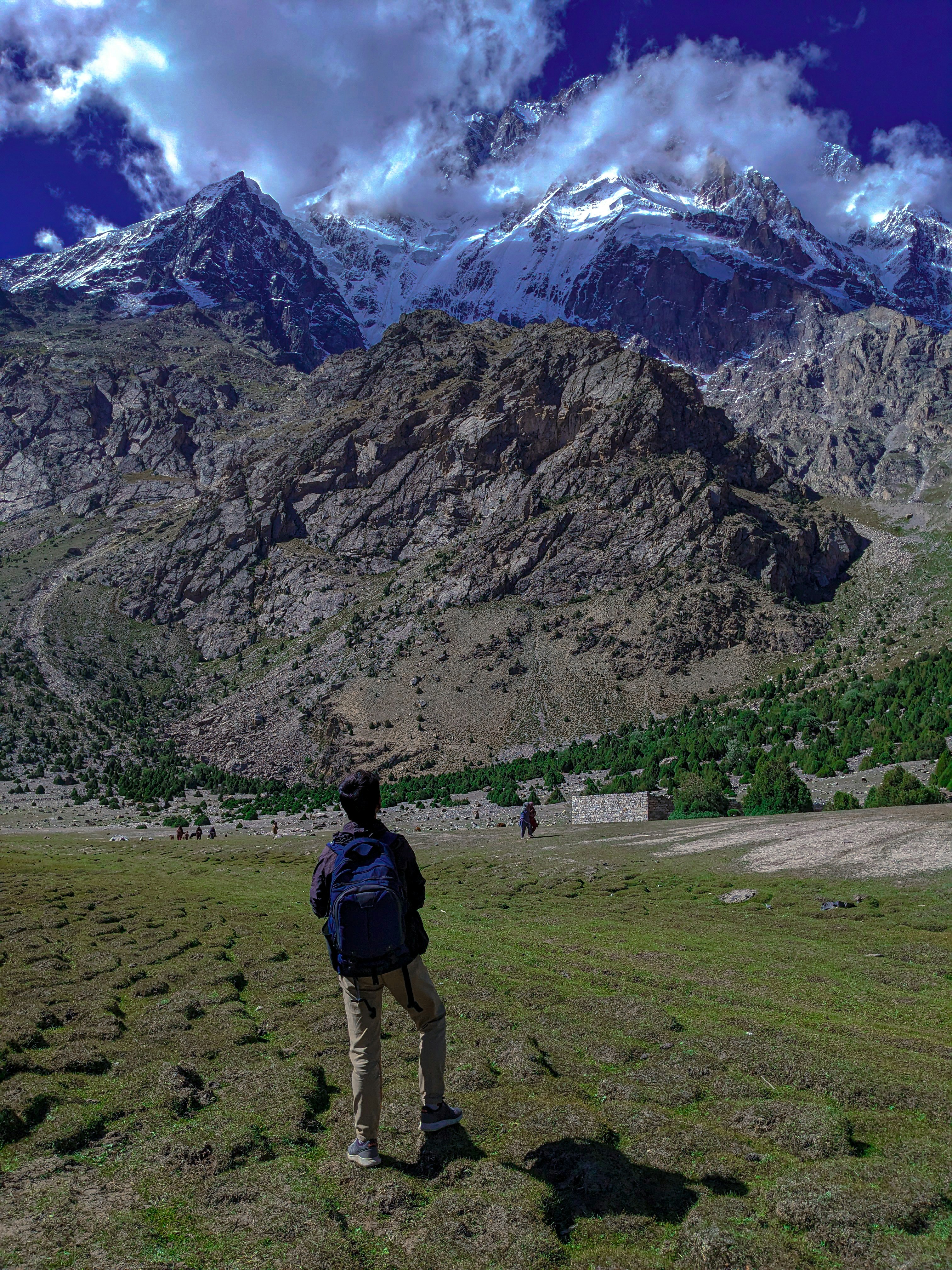 Hiker with backpack on mountain trail, bright summer day, dramatic alpine scenery