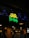 A restaurant sign reads 'Geeta Pav Bhaji' in bright yellow and green letters. Blue decorative lights are strung around the sign, adding a festive appearance. The background shows a wooden exterior with warm lighting overhead, suggesting an inviting atmosphere. People are partially visible, indicating activity inside the establishment.
