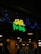 A restaurant sign reads 'Geeta Pav Bhaji' in bright yellow and green letters. Blue decorative lights are strung around the sign, adding a festive appearance. The background shows a wooden exterior with warm lighting overhead, suggesting an inviting atmosphere. People are partially visible, indicating activity inside the establishment.