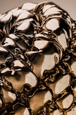 A close-up of a highly reflective, metallic surface with intricate folds and creases, giving it a fluid-like appearance. The surface captures and reflects light, creating varying shades and highlights.