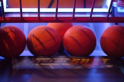 Several basketballs are aligned in a row on a basketball arcade machine platform. The environment has a colorful and illuminated backdrop with a mix of red and blue lighting.