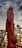 A towering statue of a mythological character, depicted in a heroic stance with intricate armor and a large mace. The background features a serene sunset with a sky of soft blues and warm oranges, framed by tall, slender trees.