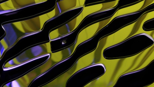 A close-up view of an abstract pattern with wavy black shapes against a bright yellow and green background. The surface appears glossy and reflective, with flowing lines and a smooth texture.