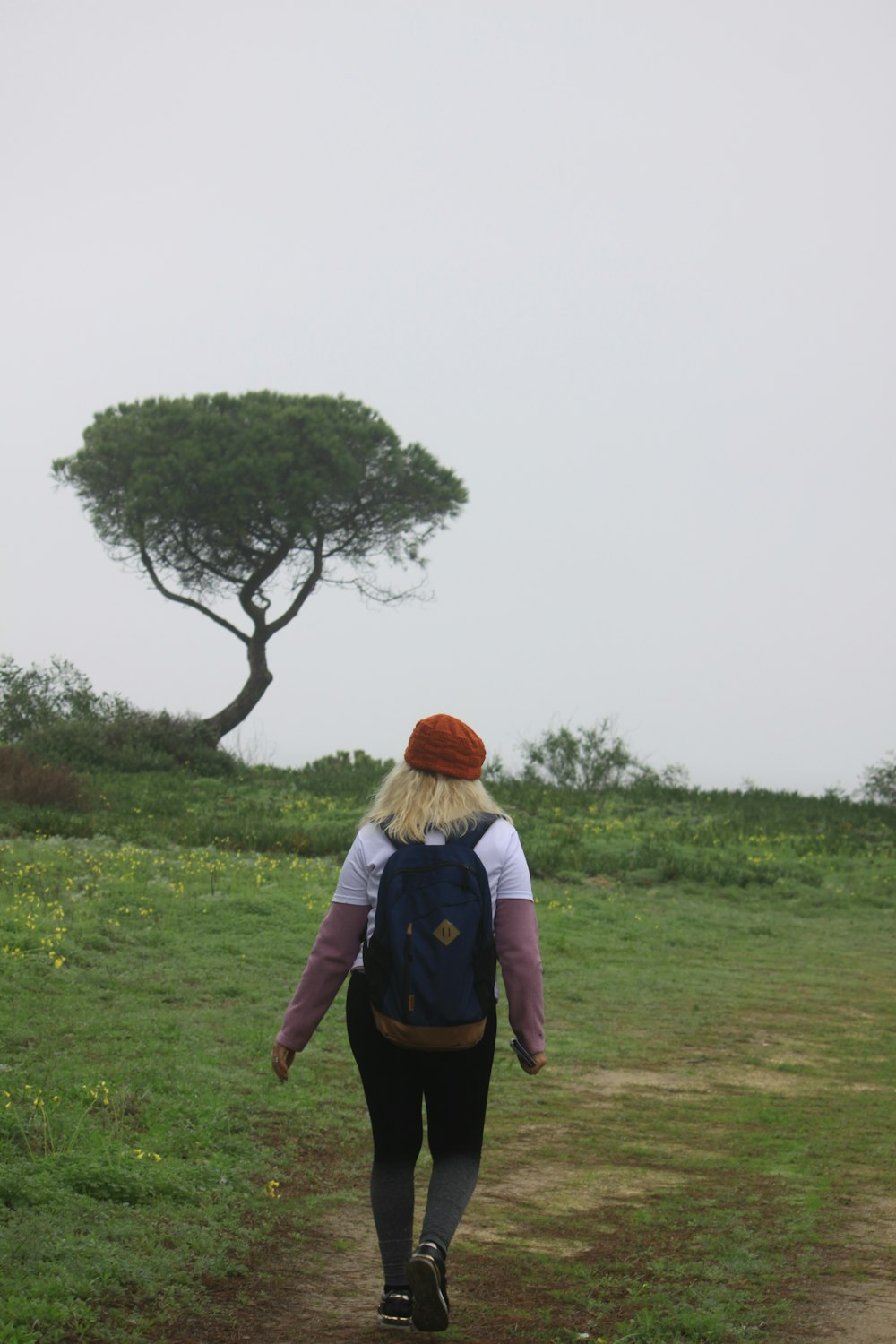 a woman walking down a dirt road with a tree in the background