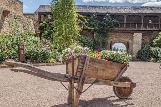 A rustic wooden garden cart filled with blooming flowers on a sunny patio.