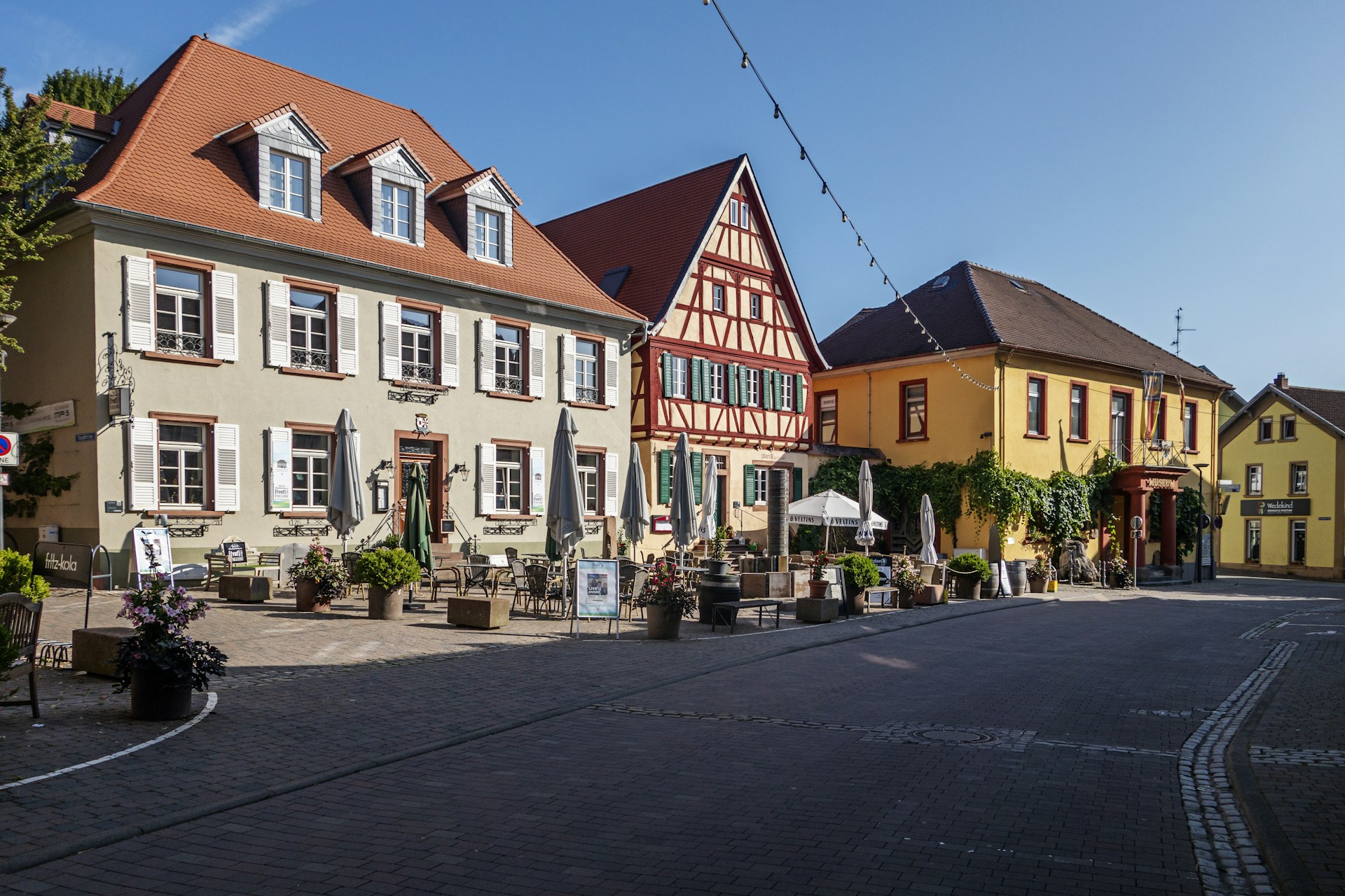A charming European village street lined with colorful buildings and vibrant flowers under a clear blue sky.