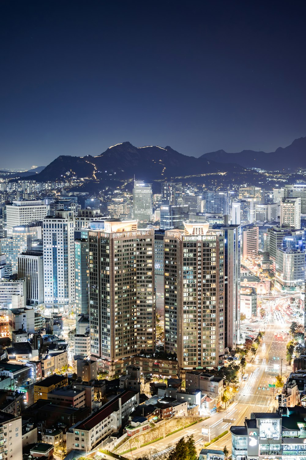 a city at night with tall buildings and mountains in the background