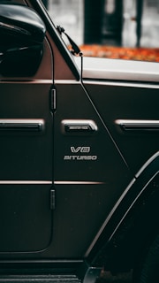 Close-up view of a dark-colored vehicle showing the side panel with visible branding, including 'AMG' and 'V8 Biturbo'. The car's side mirror and a distinctive black strip or cable are also noticeable.