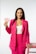 A person stands confidently against a plain backdrop wearing a bright pink blazer and pants with a white top. The person is holding two paper cards in one hand and resting the other hand on a pink stool. They have long dark hair and are smiling slightly.