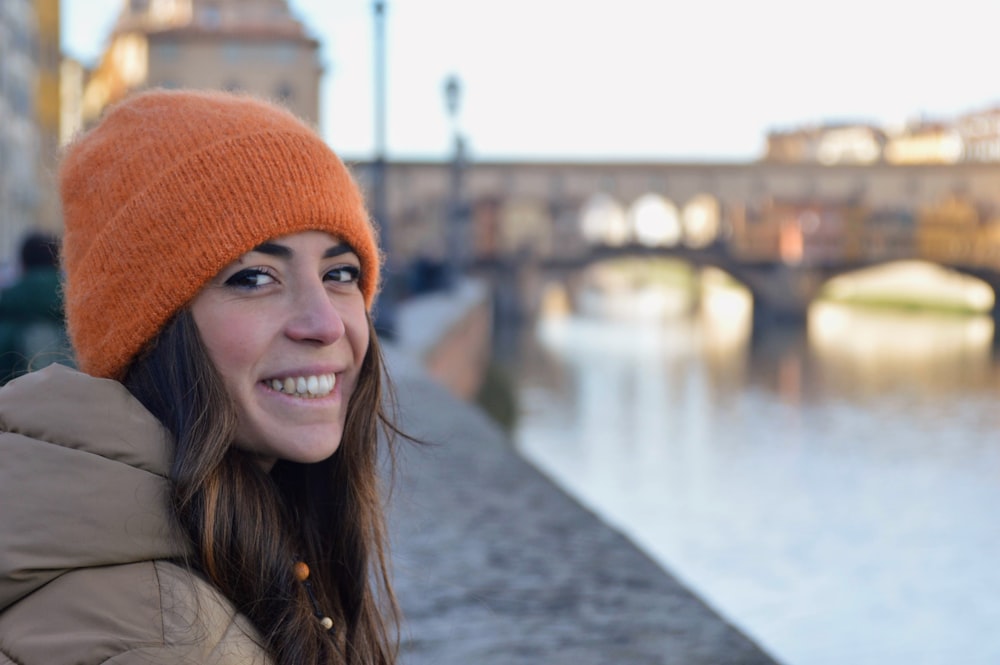 a woman wearing a orange knitted hat next to a river