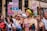 A lively group of people participating in a parade or march, holding colorful signs with messages supporting transgender rights. One sign reads 'Trans is a gift, not a disorder' while another states 'Trans lesbians are valid and really hot too.' The participants are dressed in vibrant clothing, with one person wearing a hat and sunglasses and another sporting neon green hair.