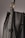 A close-up of a leather bag highlighting its textured dark material with white stitching. The bag features a gold-colored ring attaching the strap with visible threading details, giving an impression of finely crafted, high-quality design.