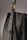 A close-up of a leather bag highlighting its textured dark material with white stitching. The bag features a gold-colored ring attaching the strap with visible threading details, giving an impression of finely crafted, high-quality design.