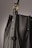 A close-up of a leather bag highlighting its textured dark material with white stitching. The bag features a gold-colored ring attaching the strap with visible threading details, giving an impression of finely crafted, high-quality design.