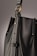 A close-up of a leather bag highlighting its textured dark material with white stitching. The bag features a gold-colored ring attaching the strap with visible threading details, giving an impression of finely crafted, high-quality design.