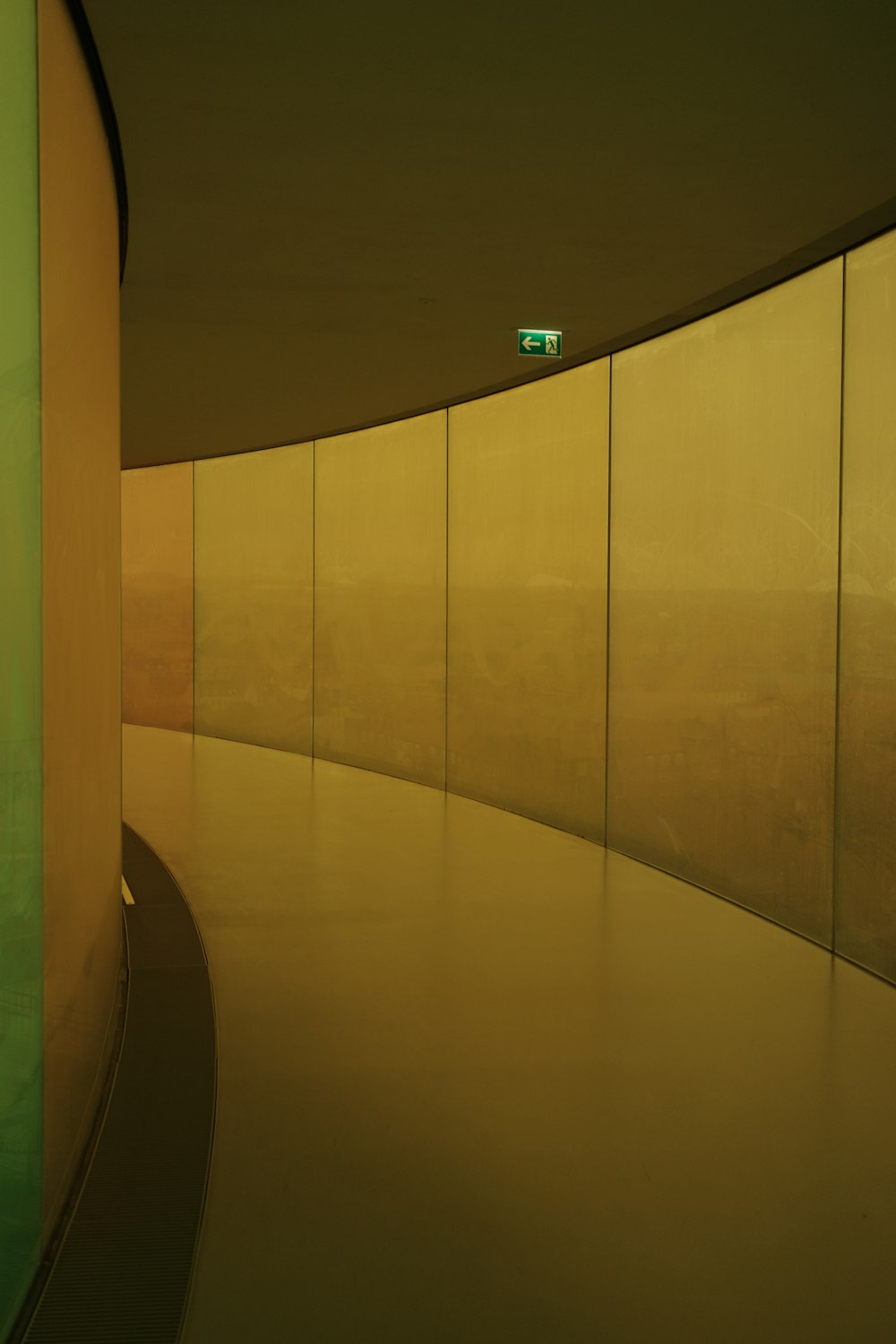 a curved walkway next to a green wall