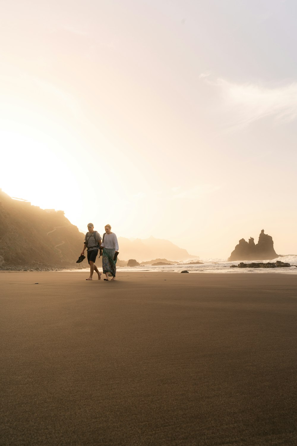 two people walking on the beach at sunset