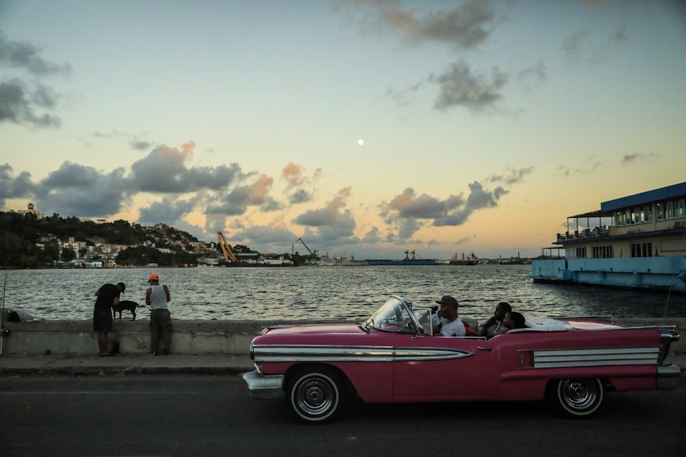 a pink car parked next to a body of water