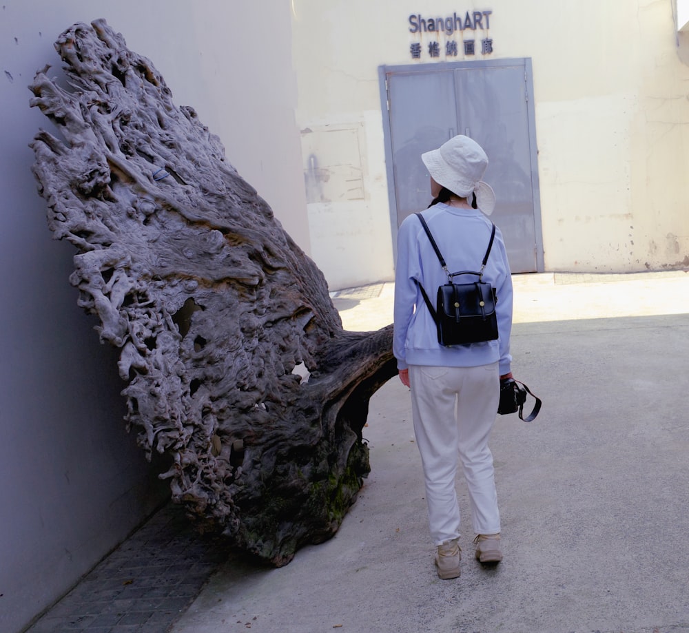 a woman in a white hat and blue shirt is walking past a large tree trunk
