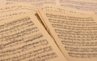 A collection of open sheet music, with musical notations and scores visible on aged paper. The sheets are slightly overlapping, suggesting a well-used and possibly vintage collection.