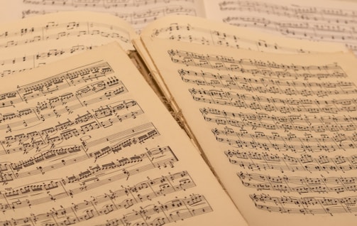 A collection of open sheet music, with musical notations and scores visible on aged paper. The sheets are slightly overlapping, suggesting a well-used and possibly vintage collection.