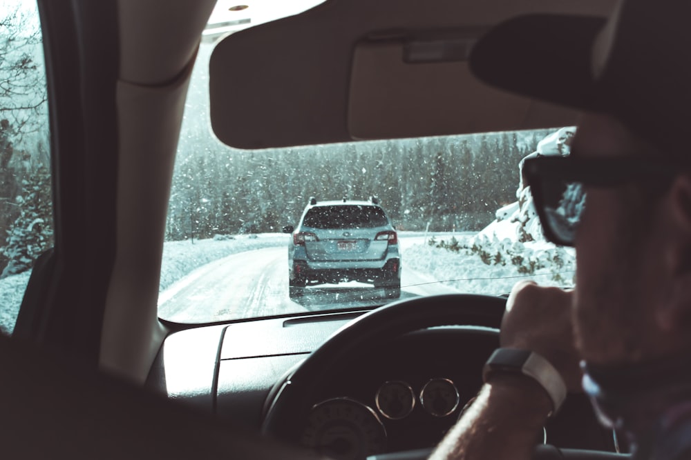 um homem dirigindo um carro em uma estrada nevada
