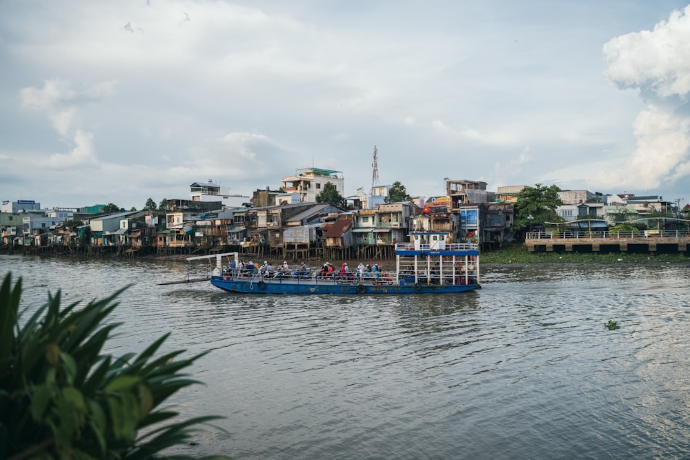 a blue boat traveling down a river next to a city