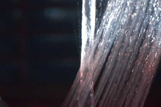 Water streams downwards in a continuous flow, illuminated by lights that create a shimmering effect. The texture and movement of the water are captured with a sense of fluidity and energy.