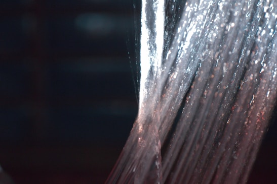 Water streams downwards in a continuous flow, illuminated by lights that create a shimmering effect. The texture and movement of the water are captured with a sense of fluidity and energy.