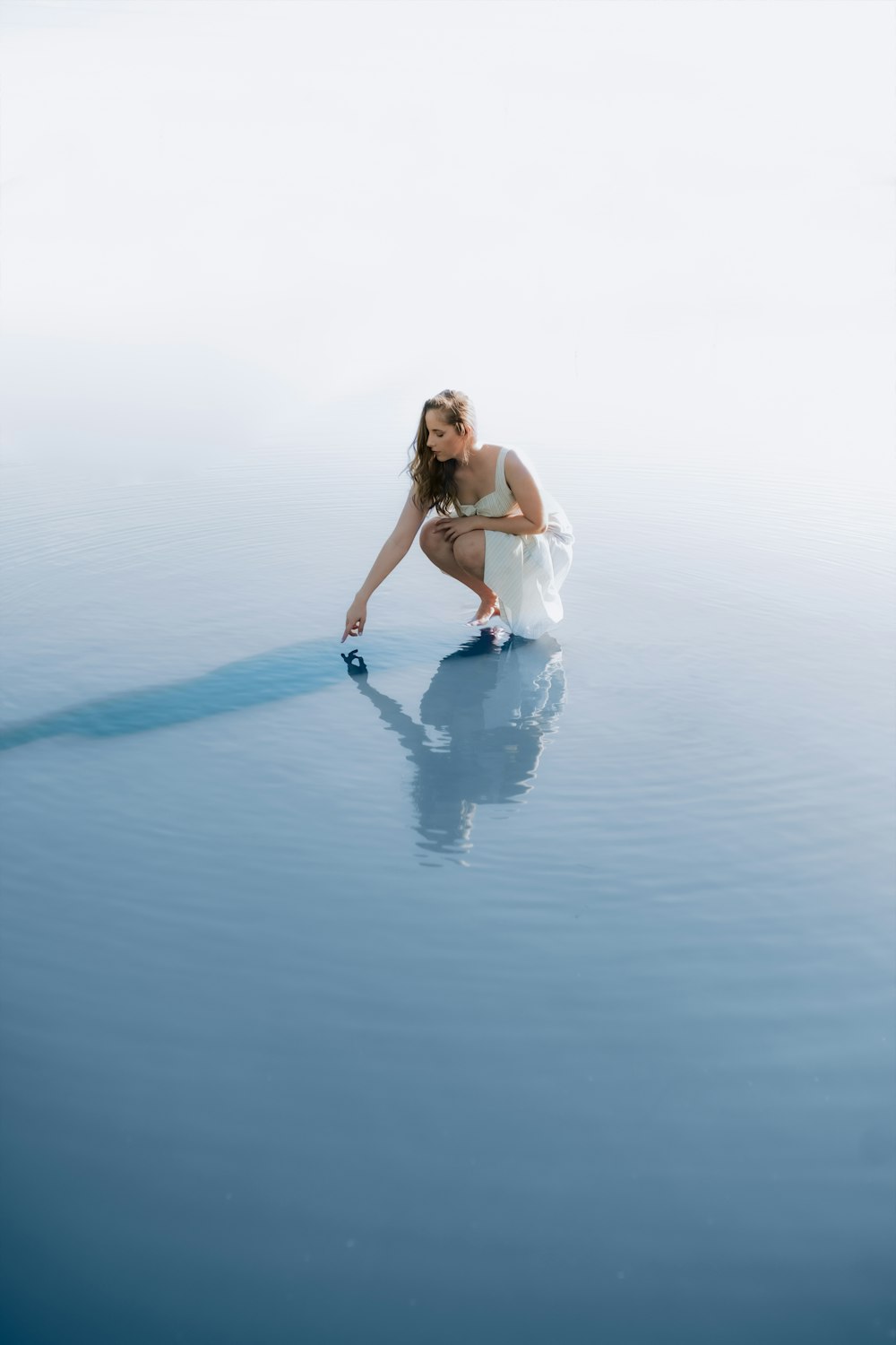 uma mulher com um vestido branco ajoelhada na água