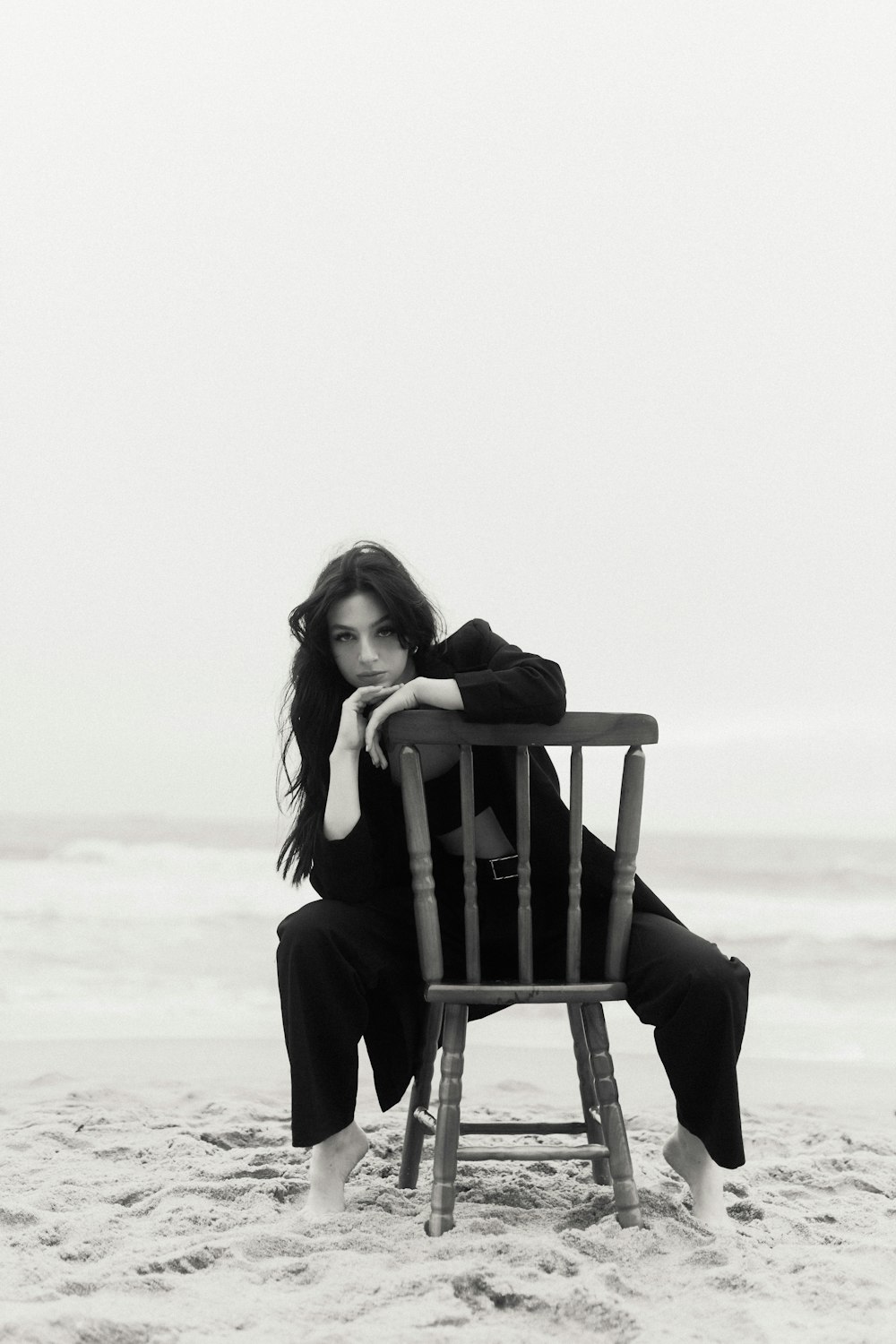 a woman sitting on top of a wooden chair on top of a beach