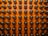 A grid of reflective capsules or vials with dark material inside, arranged on an orange background. They are organized in neat rows, with each having a shiny, rounded top.