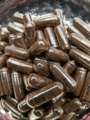 A collection of transparent capsules filled with a brown powdery substance. The capsules are densely packed together, creating a textured appearance.