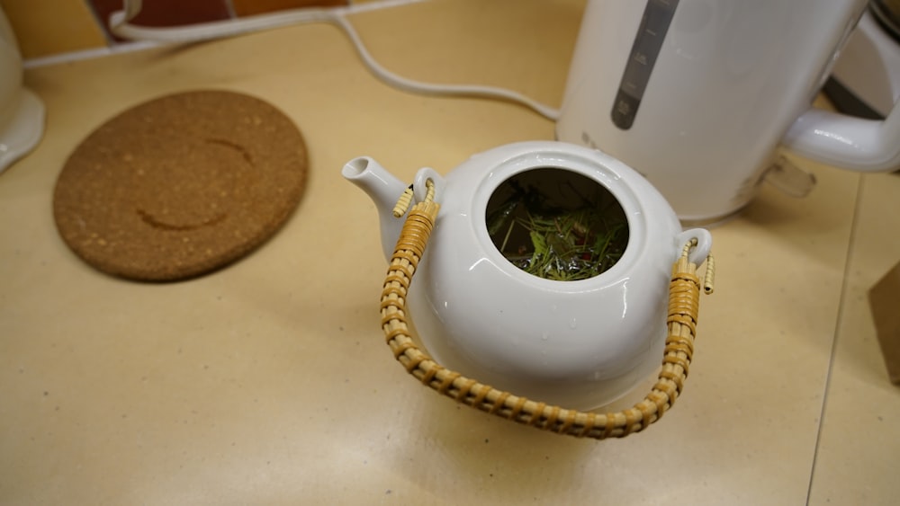 a white teapot with a green plant inside of it