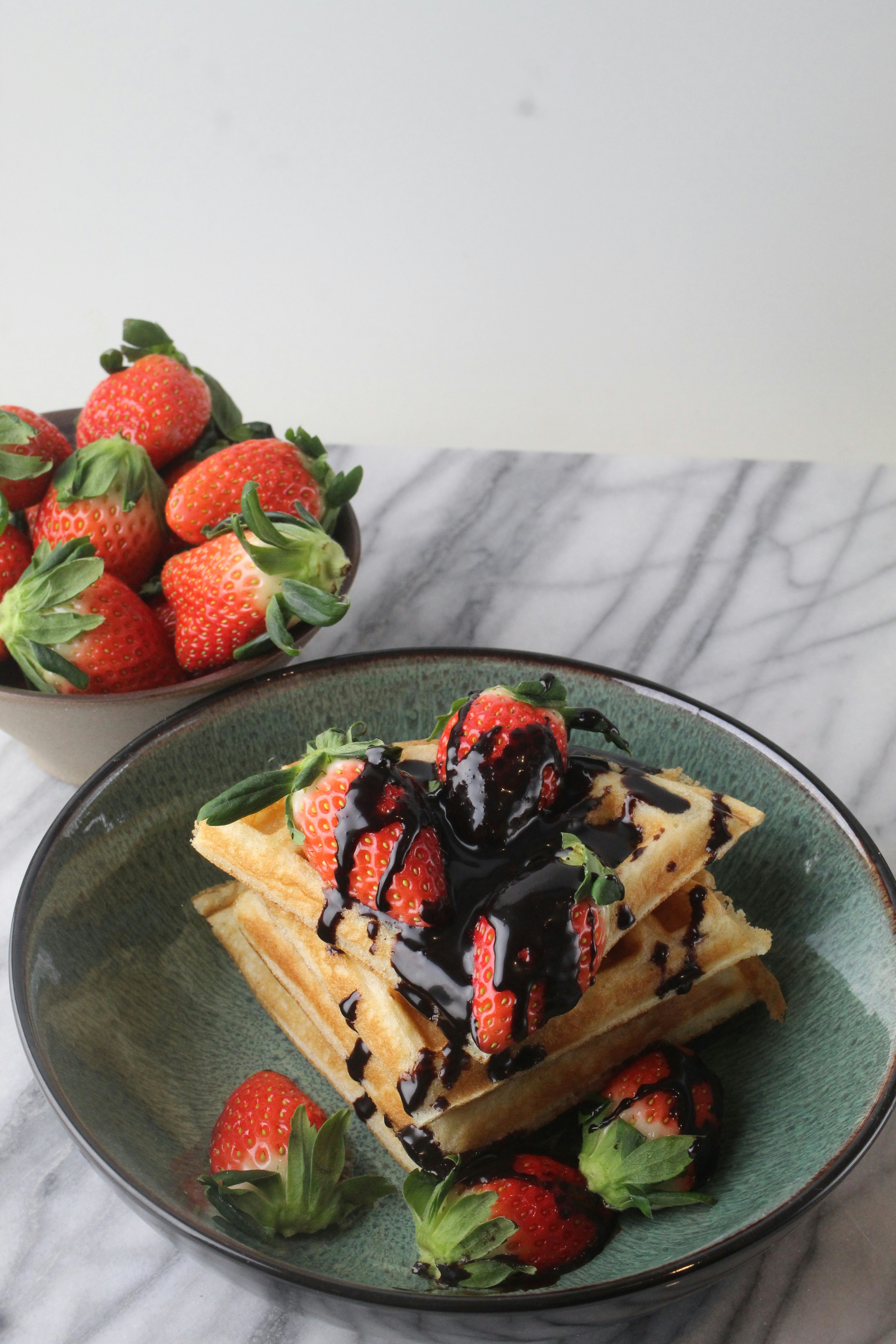 a plate of waffles with chocolate sauce and strawberries