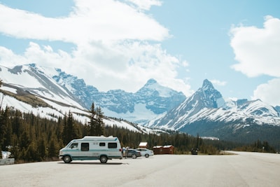 An all-terrain RV parked in a snowy mountain landscape under a bright blue sky.
