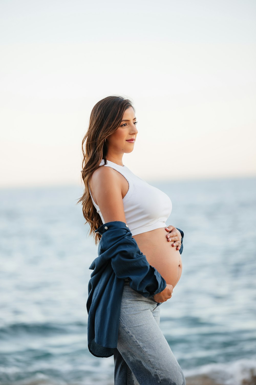 a pregnant woman standing on a beach next to the ocean