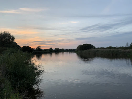 A serene view of the Missouri River flowing gently past lush riverbanks at sunset.