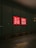 A dark street with a large glass window featuring a bright red and white UNIQLO logo, illuminated against the dark surroundings. The arrow painted on the pavement in the foreground points towards the glass wall.
