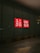 A dark street with a large glass window featuring a bright red and white UNIQLO logo, illuminated against the dark surroundings. The arrow painted on the pavement in the foreground points towards the glass wall.