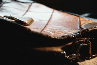Close-up of a textured leather handbag with visible stitching and metallic elements, partially illuminated by light.