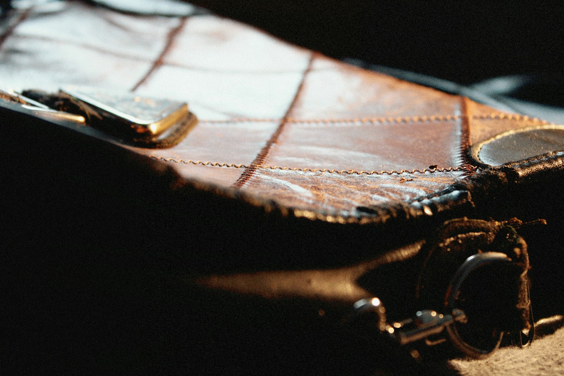 Close-up of a textured leather handbag with visible stitching and metallic elements, partially illuminated by light.
