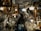 A person stands in a cluttered antique store filled with various vintage items. The shelves and walls are adorned with ornate picture frames, decorative plates, and glassware. Chandeliers and lamps hang from the ceiling, casting a warm glow over the scene.