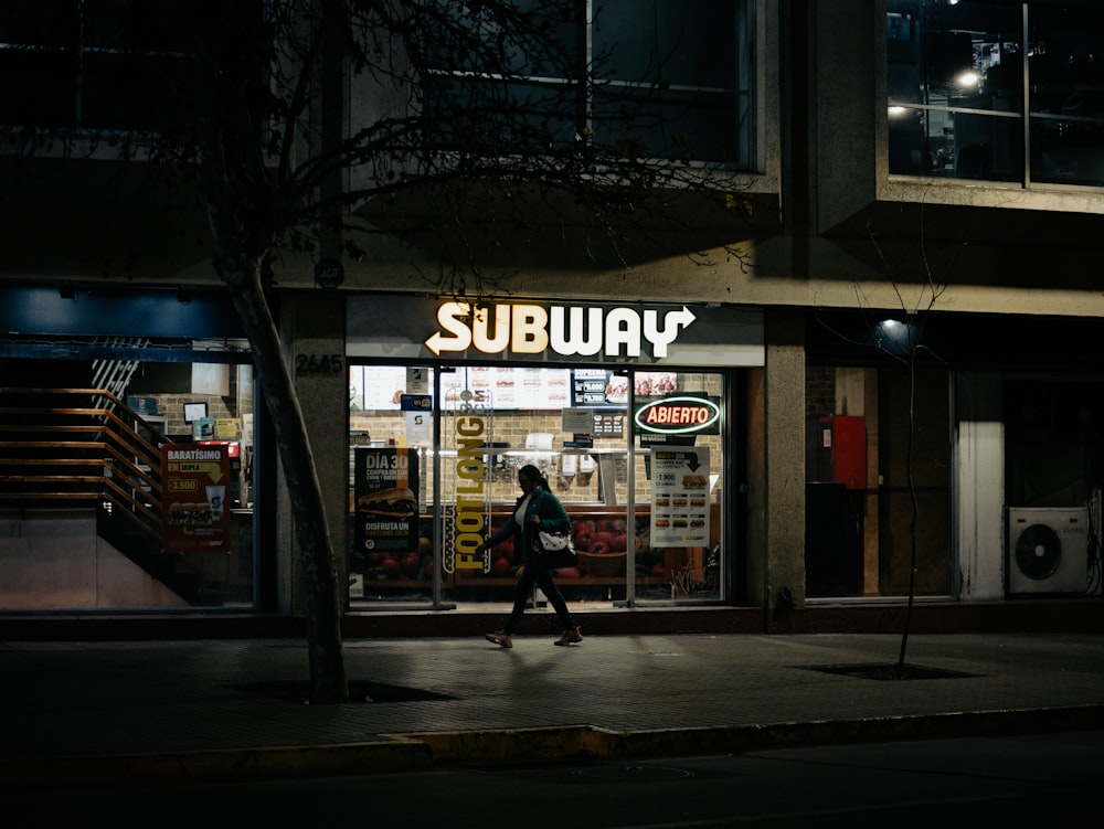 a woman walking past a subway store at night